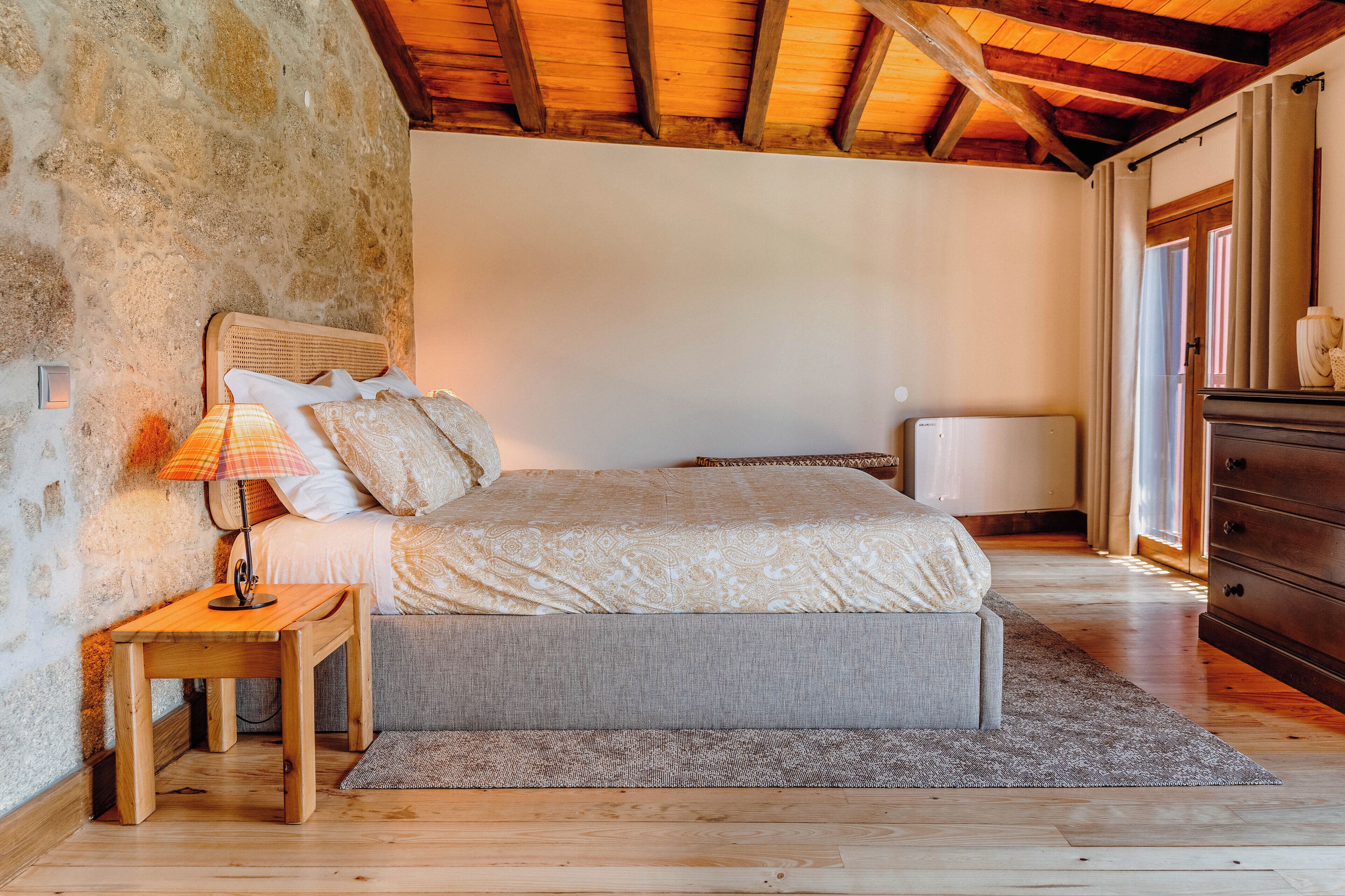 A bedroom with a bed, bedside table, lamp, and a dresser.