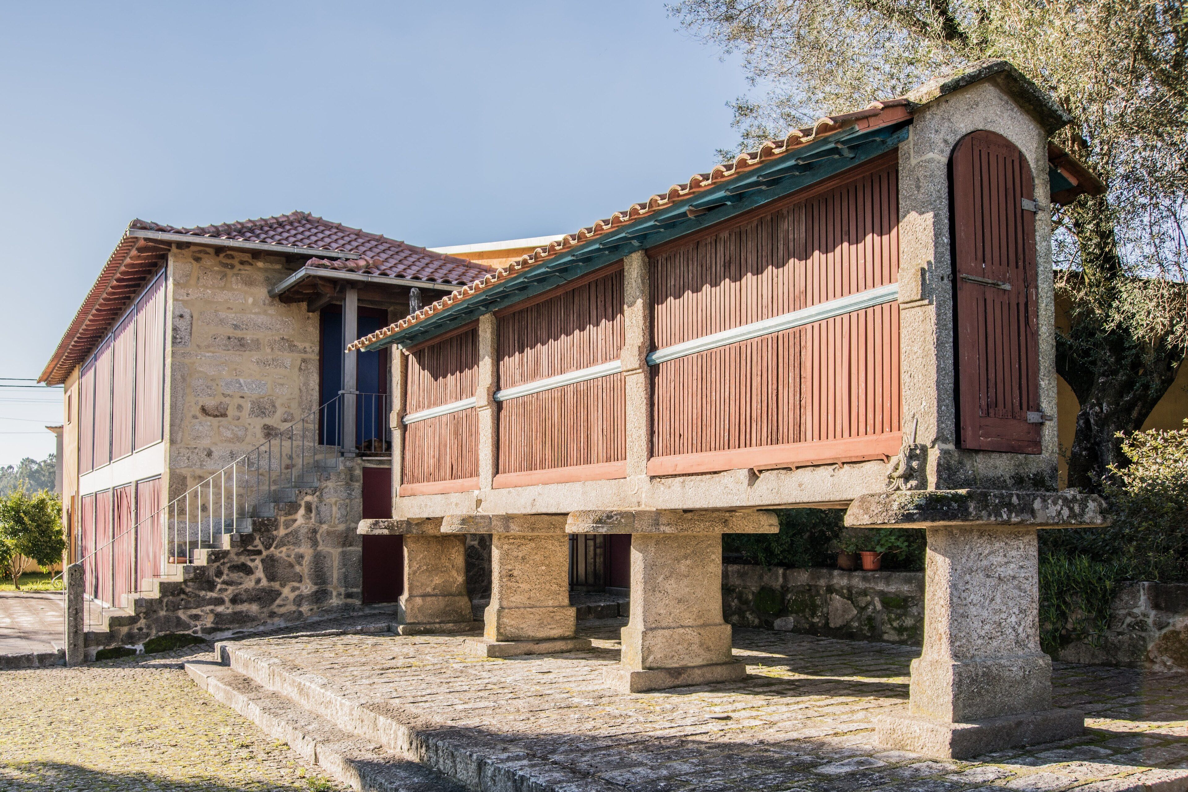Un edificio de piedra con techo de tejas y contraventanas de madera, que presenta una escalera de piedra que conduce a un nivel superior.