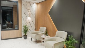Un espace d’accueil moderne avec des murs en marbre, deux fauteuils, une petite table ronde et des plantes en pot.