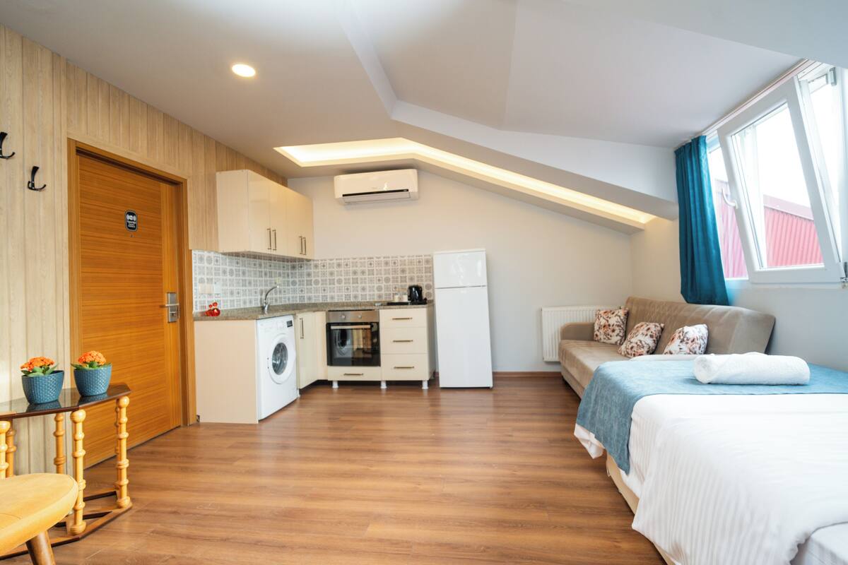 Una habitación compacta con kitchenette, cama y espacio para sentarse.