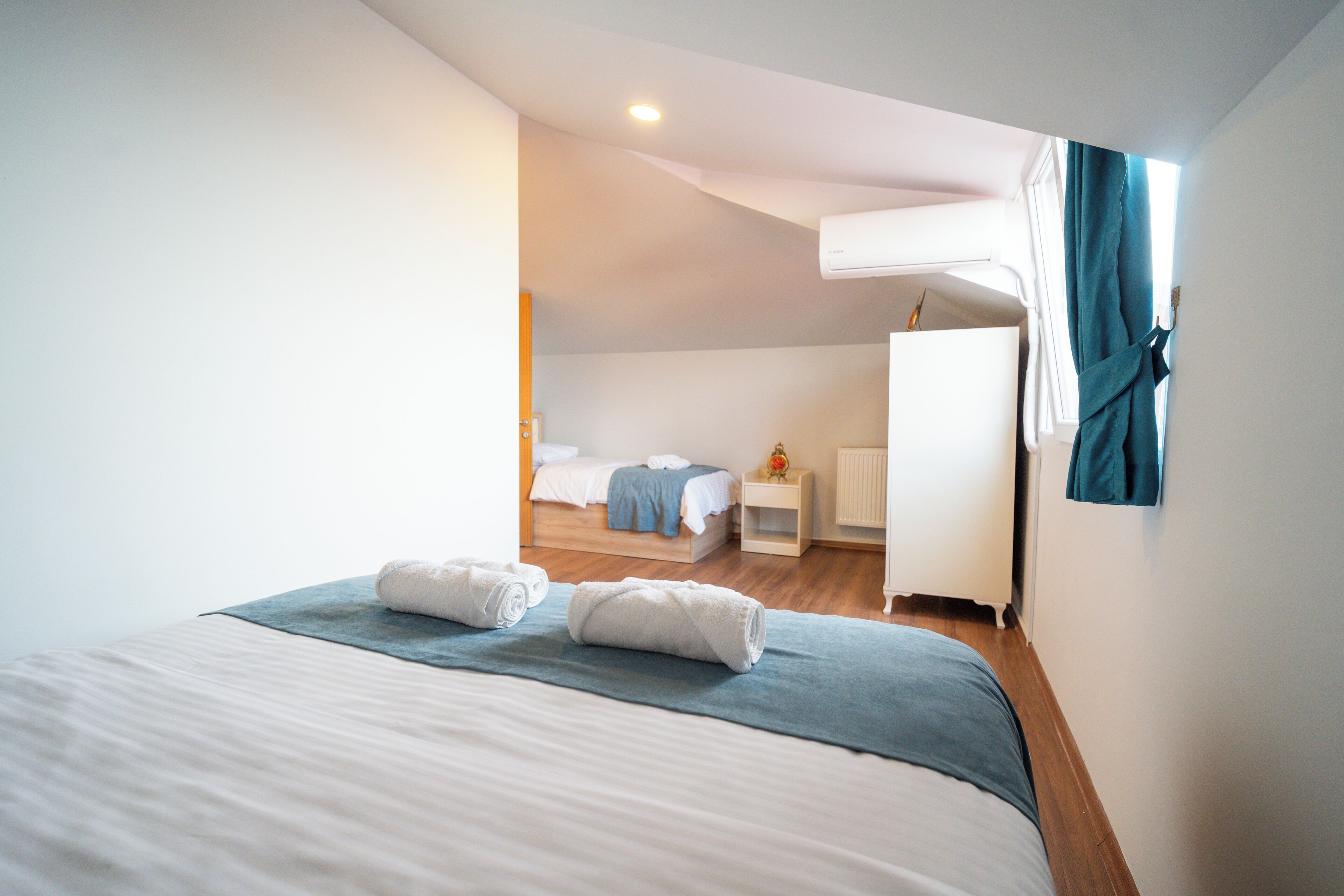 Een slaapkamer met een bed, nachtkastje, dressoir en een raam met gordijnen.