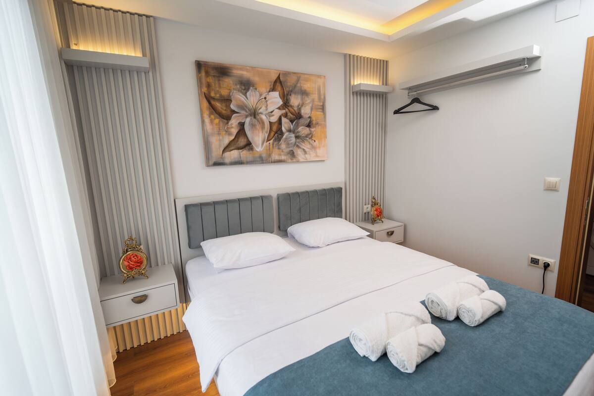 Una habitación de hotel moderna con una cama grande, una mesita de noche con lámpara, aire acondicionado en la pared y un cuadro sobre la cama.
