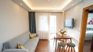 Une chambre d’hôtel moderne avec un canapé gris, une table à manger en bois et deux chaises vertes.