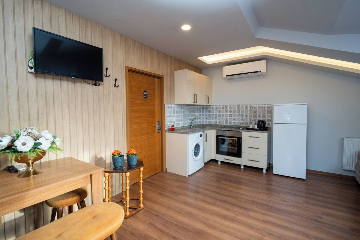Una cocina compacta con lavadora, refrigerador y televisor instalado en la pared.