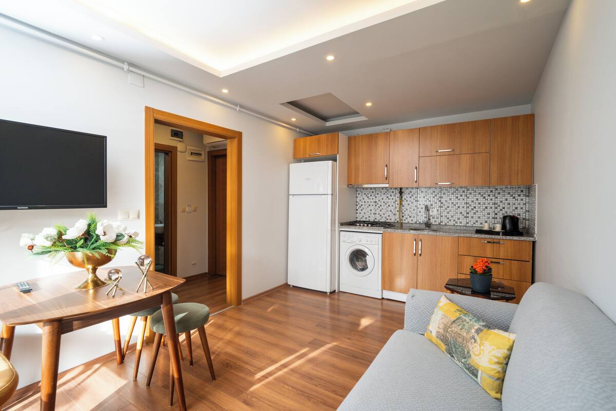 Un espacio habitable compacto con comedor, kitchenette y un sofá con cojines.