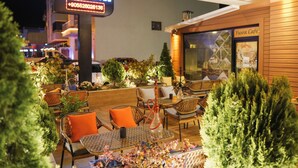 Un espace extérieur aménagé avec des meubles en osier et des coussins orange, un narguilé et une enseigne indiquant « Yusra Apart Hotel ».