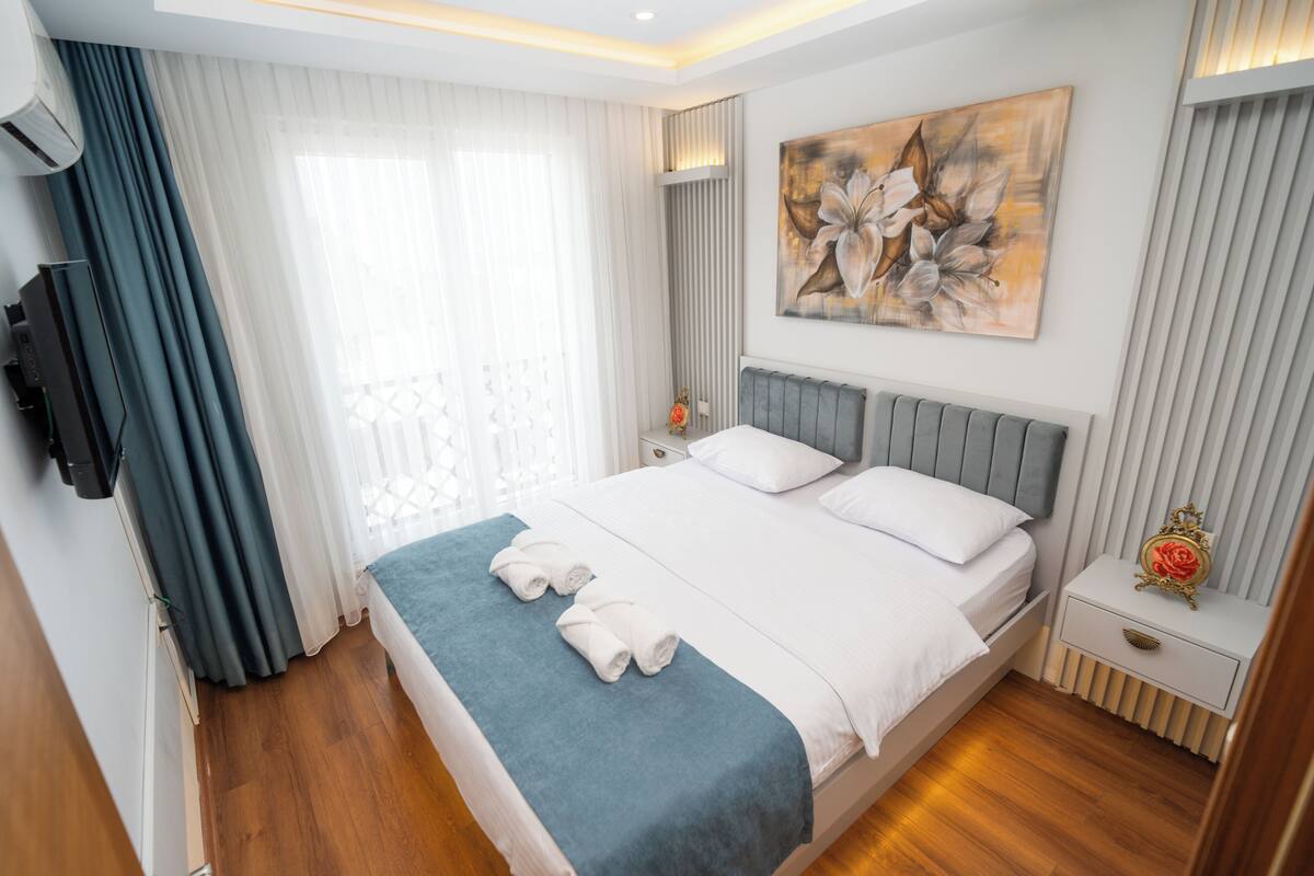 Una habitación de hotel moderna con una cama grande, un televisor de pantalla plana montado en la pared y un cuadro sobre la cama.