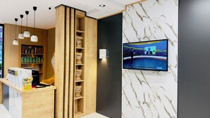 Un espace d’accueil moderne avec un comptoir en bois, des étagères remplies de produits et un téléviseur fixé au mur diffusant un journal télévisé.