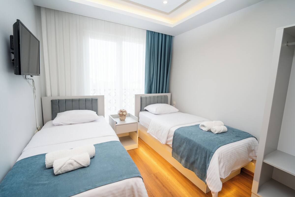 Habitación de hotel con dos camas individuales, un televisor de pantalla plana en la pared y una ventana con cortinas.