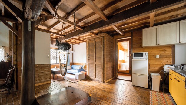 A rustic interior with wooden floors, a dining area, a kitchen with white cabinets, and a hanging light fixture. - Sennin Cabin Hakuba (Hakuba)