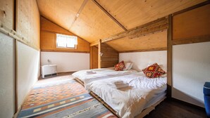 A bedroom with a sloped ceiling, a window, a bed with white linens, a colorful rug, and a small heater. - Sennin Cabin Hakuba (Hakuba)