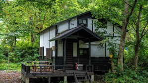 A traditional wooden structure with a porch, surrounded by dense forest. - Sennin Cabin Hakuba (Hakuba)
