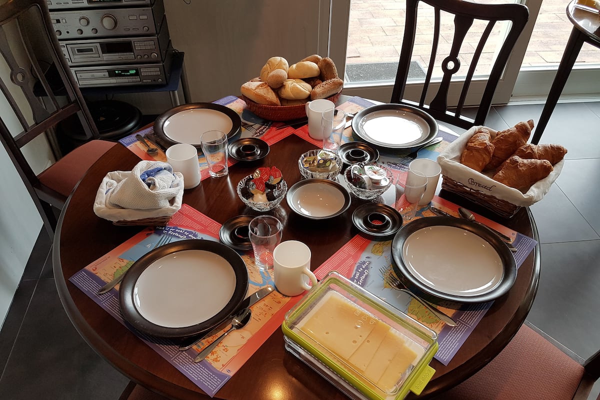 Een eettafel gedekt met borden, kommen, glazen en diverse soorten eten, waaronder brood en gebak.