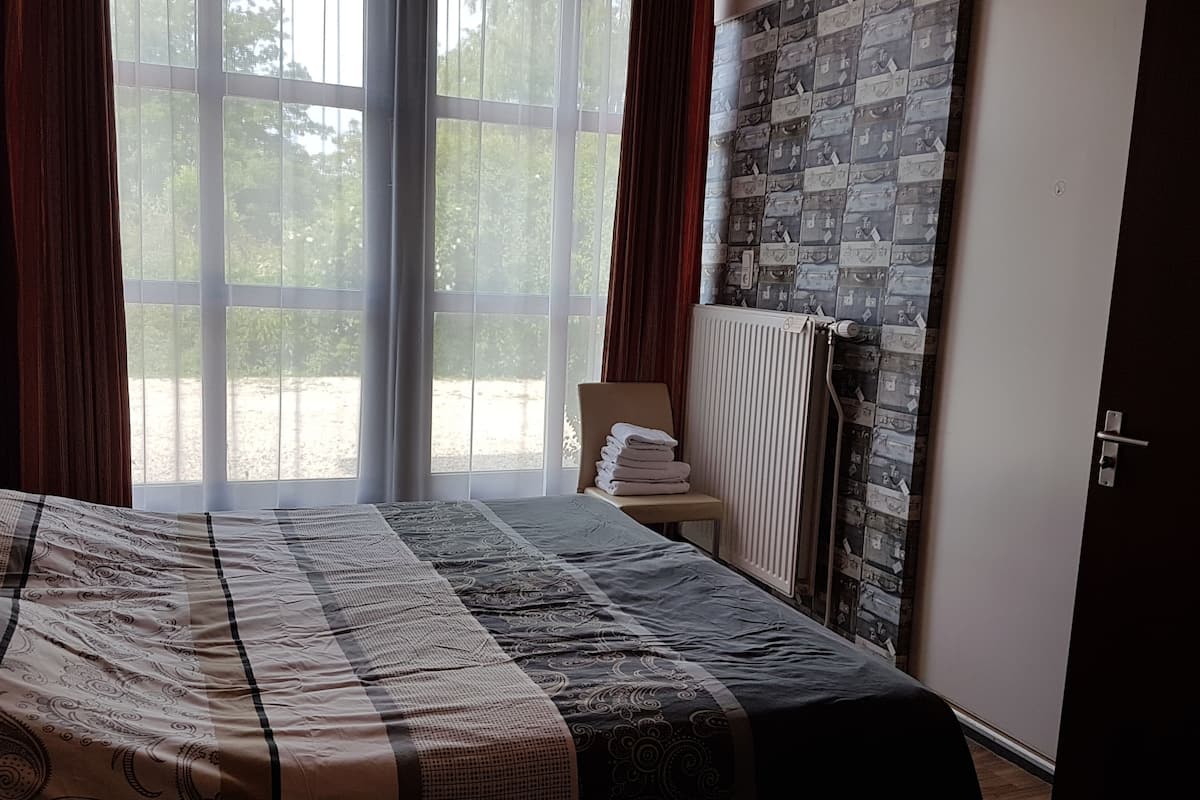 Een slaapkamer met een groot bed, een radiator en uitzicht door een raam.