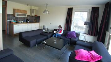 A modern living room with a black sofa, a glass coffee table, and a person reading a book.
