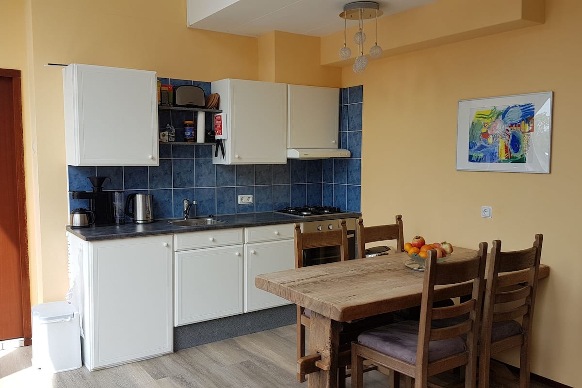 Een compacte keuken met witte kasten, een gasfornuis en een eettafel met stoelen.
