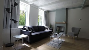 Ett modernt vardagsrum med en mörk soffa, ett soffbord, ett sidobord, en fåtölj och en öppen spis.