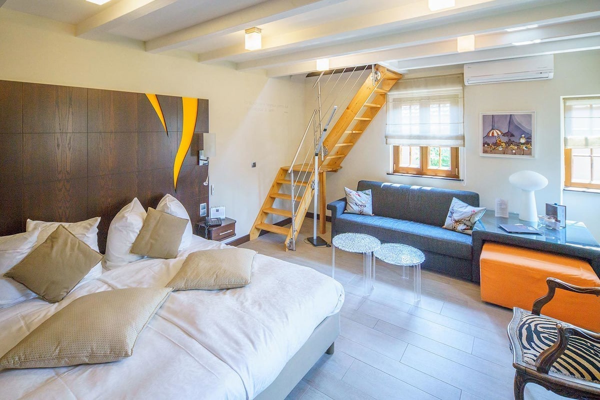 Un dormitorio con una cama grande, un sofá, una mesita y una escalera que sube a un nivel superior.