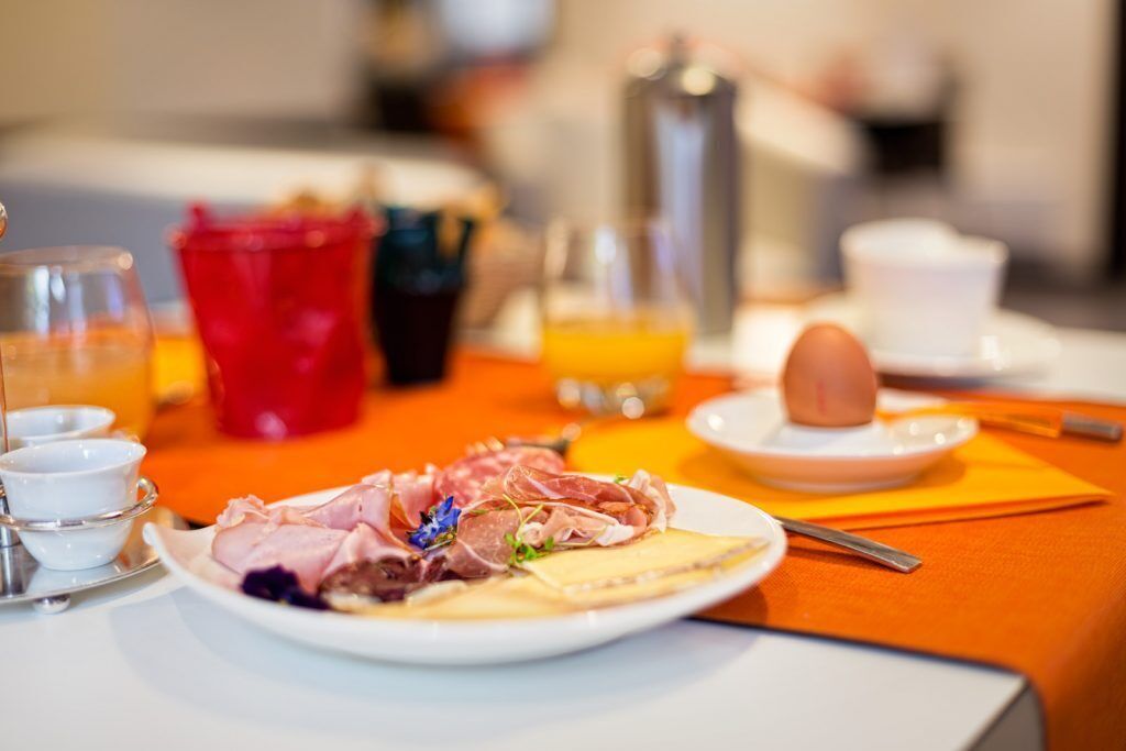Ein Frühstückstisch mit Wurst, Käse und einem gekochten Ei, dazu Orangensaft und Kaffeetassen.