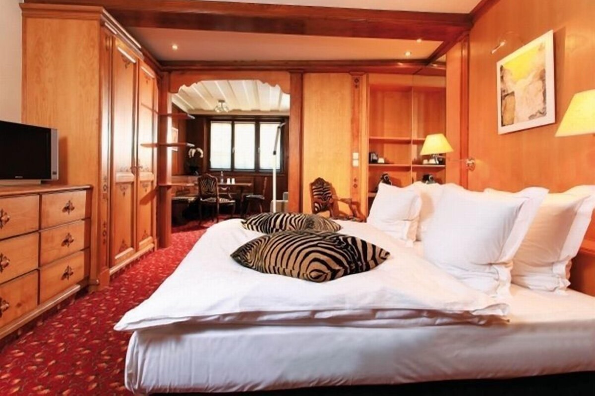 A hotel room with a large bed, wooden wardrobe, desk, and chair.