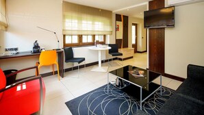 A modern living room with a round dining table, two black chairs, a red chair, a black sofa, and a flat-screen TV mounted on the wall. - Hotel Restaurant & Spa - Le Cerf (Marlenheim)
