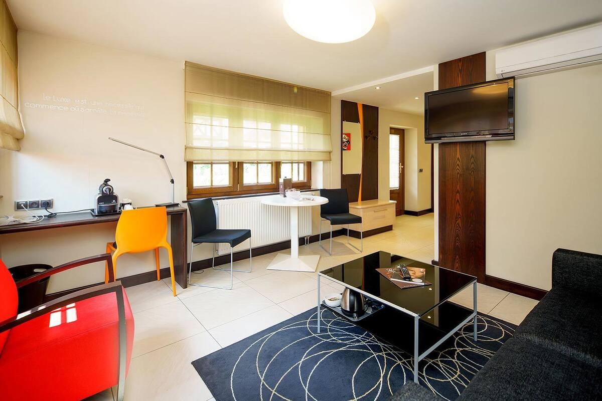 Una sala moderna con una mesa redonda de comedor, dos sillas negras, una silla roja, un sofá negro y un televisor de pantalla plana montado en la pared.