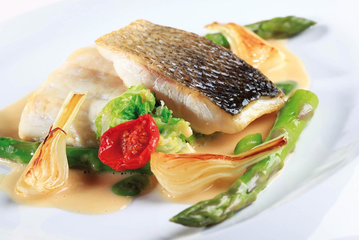 Een bord met vis, asperges en een rode peper.