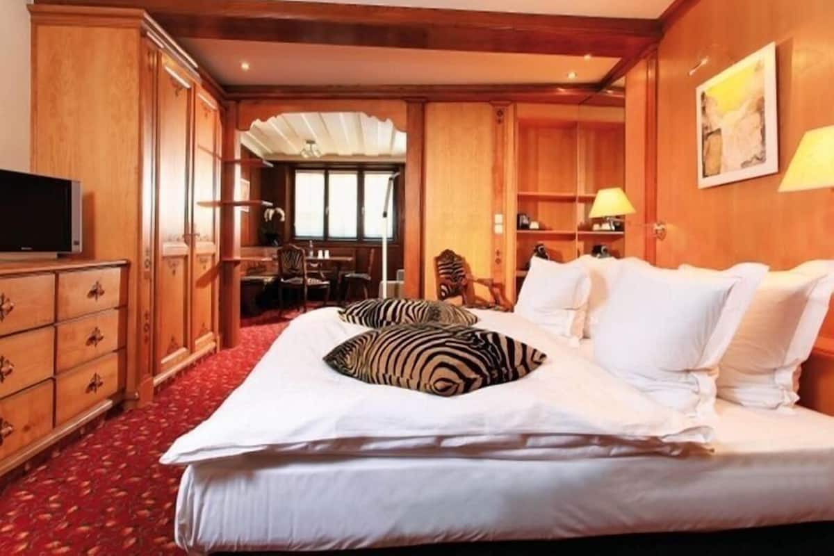 Habitación de hotel con una cama grande, armario de madera, escritorio y silla.