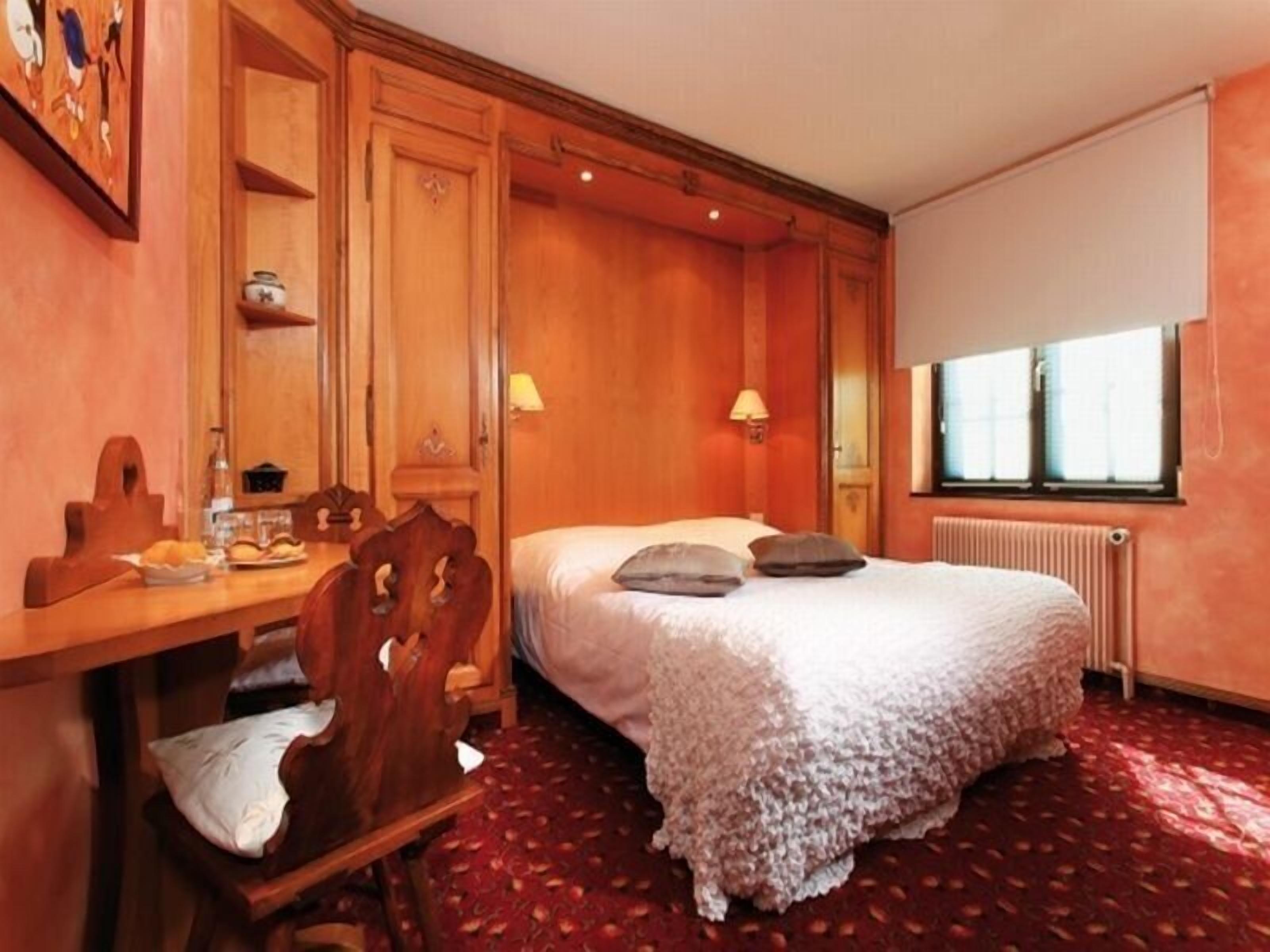 Ein Schlafzimmer mit Bett, Schreibtisch aus Holz, Stuhl und Fenster.