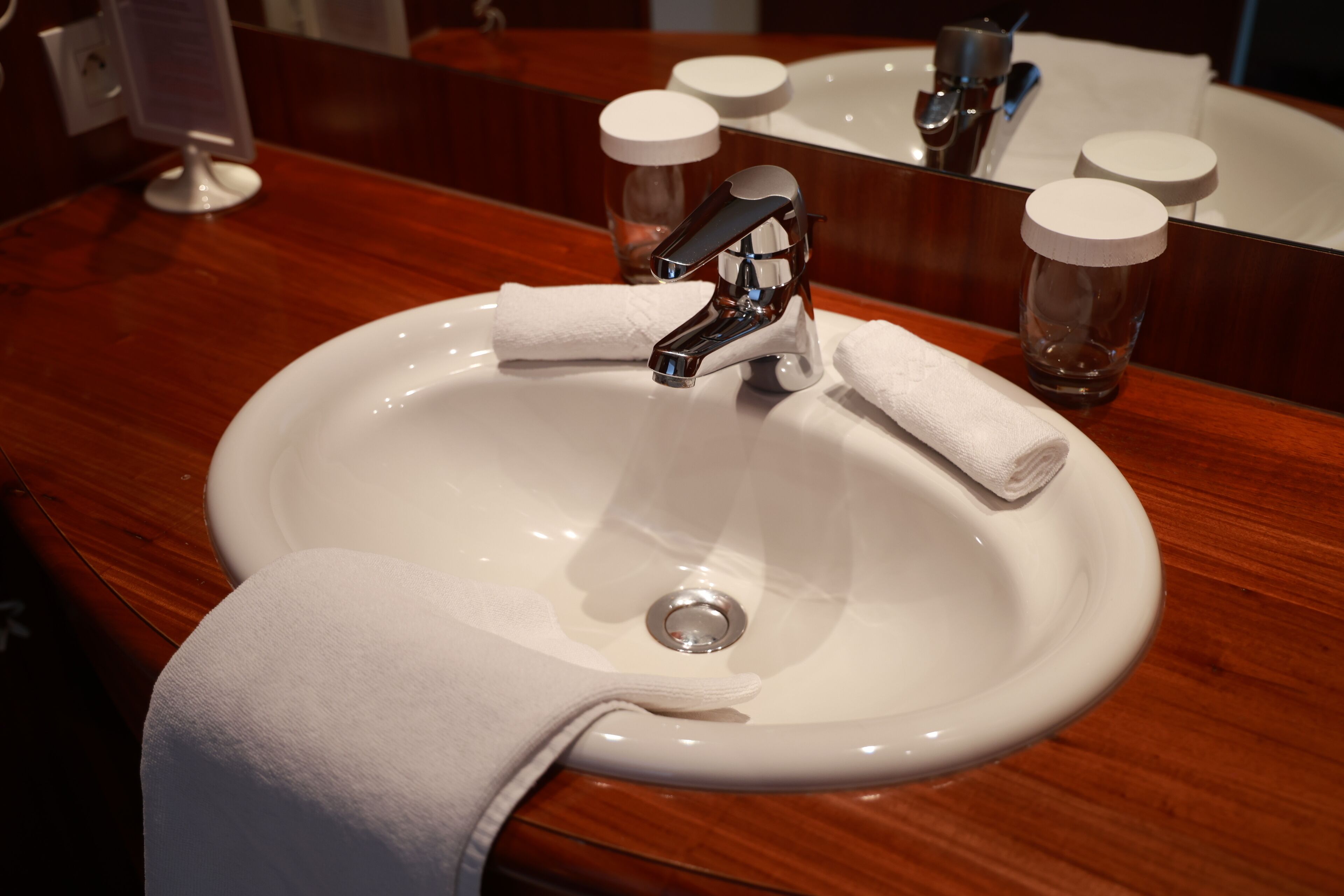A white sink with a chrome faucet, a white towel, and two glass bottles with white lids on a wooden countertop.