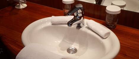 A white sink with a chrome faucet, a white towel, and two glass bottles with white lids on a wooden countertop.
