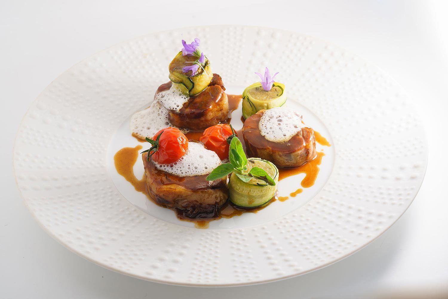 A plate of food with various dishes, including a piece of meat with sauce and garnishes, and a vegetable dish with a flower on top.