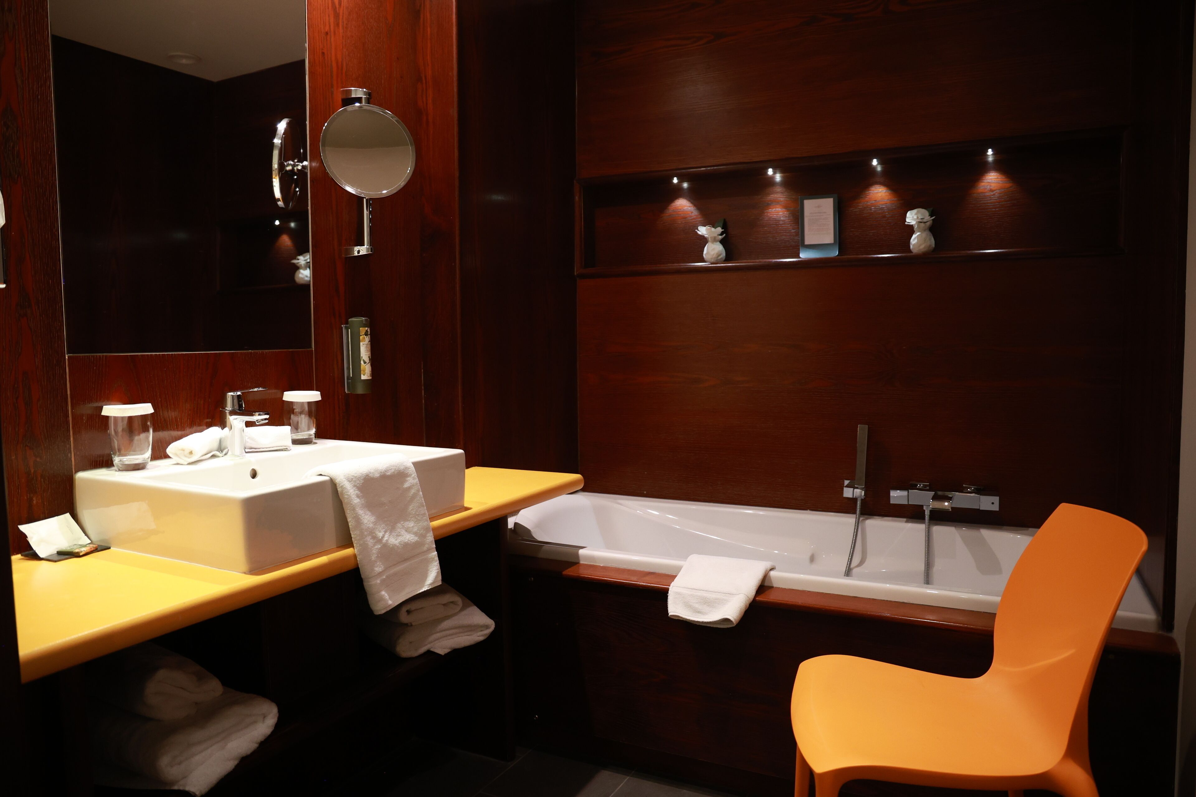 A modern bathroom with two sinks, a bathtub, and an orange chair.
