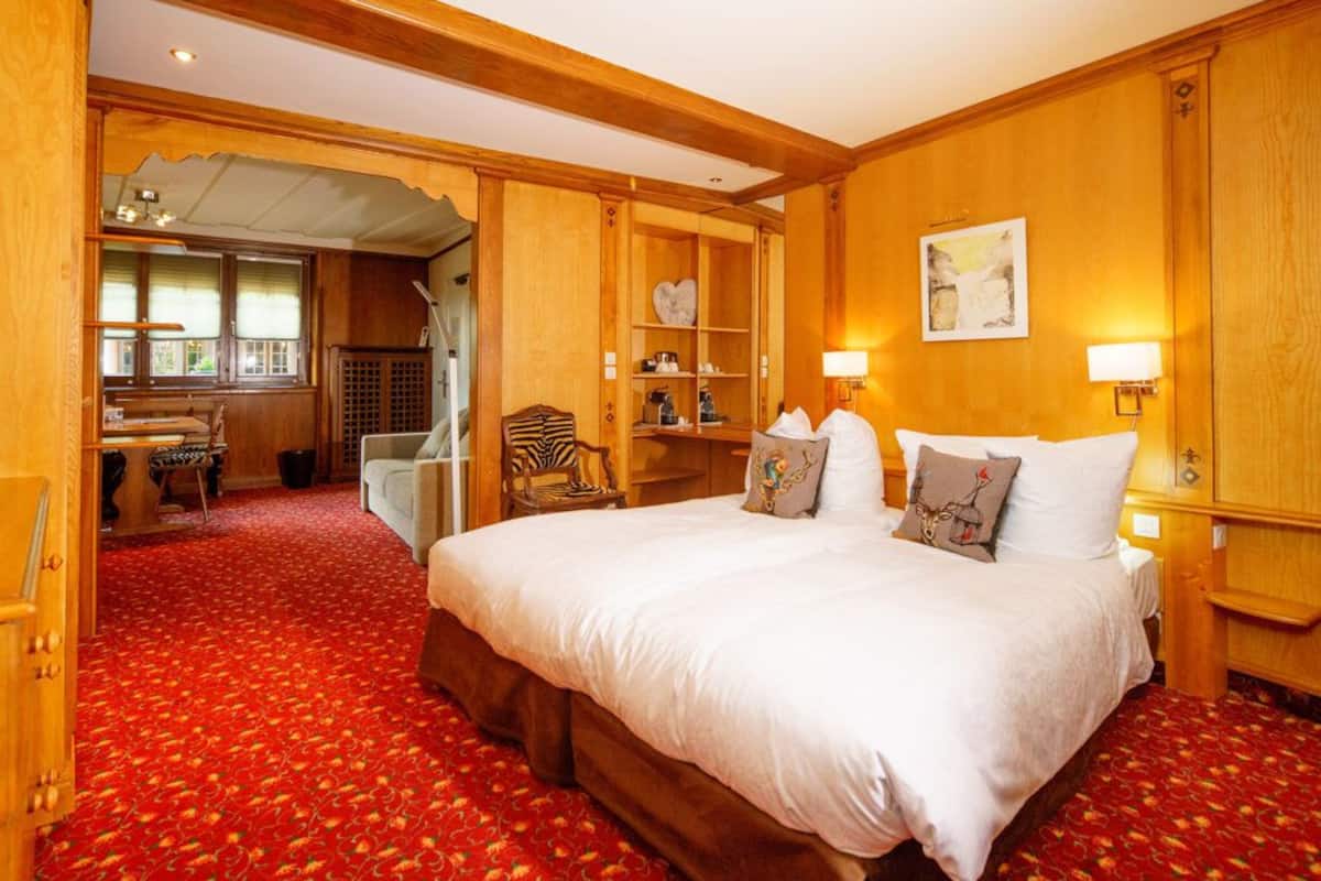 Habitación de hotel con una cama grande, paneles de madera, alfombra roja y una pequeña zona de estar con una mesa y sillas.