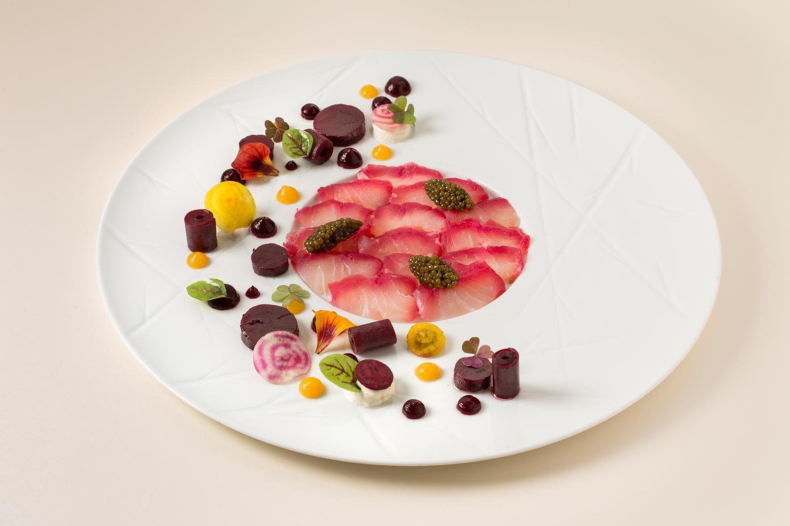 A white plate with a variety of food items including slices of pink meat, green leaves, and small round objects.