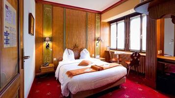 Une chambre d’hôtel avec un grand lit, deux tables de chevet, un bureau et une chaise. Il y a deux lampes murales et une fenêtre avec des rideaux.