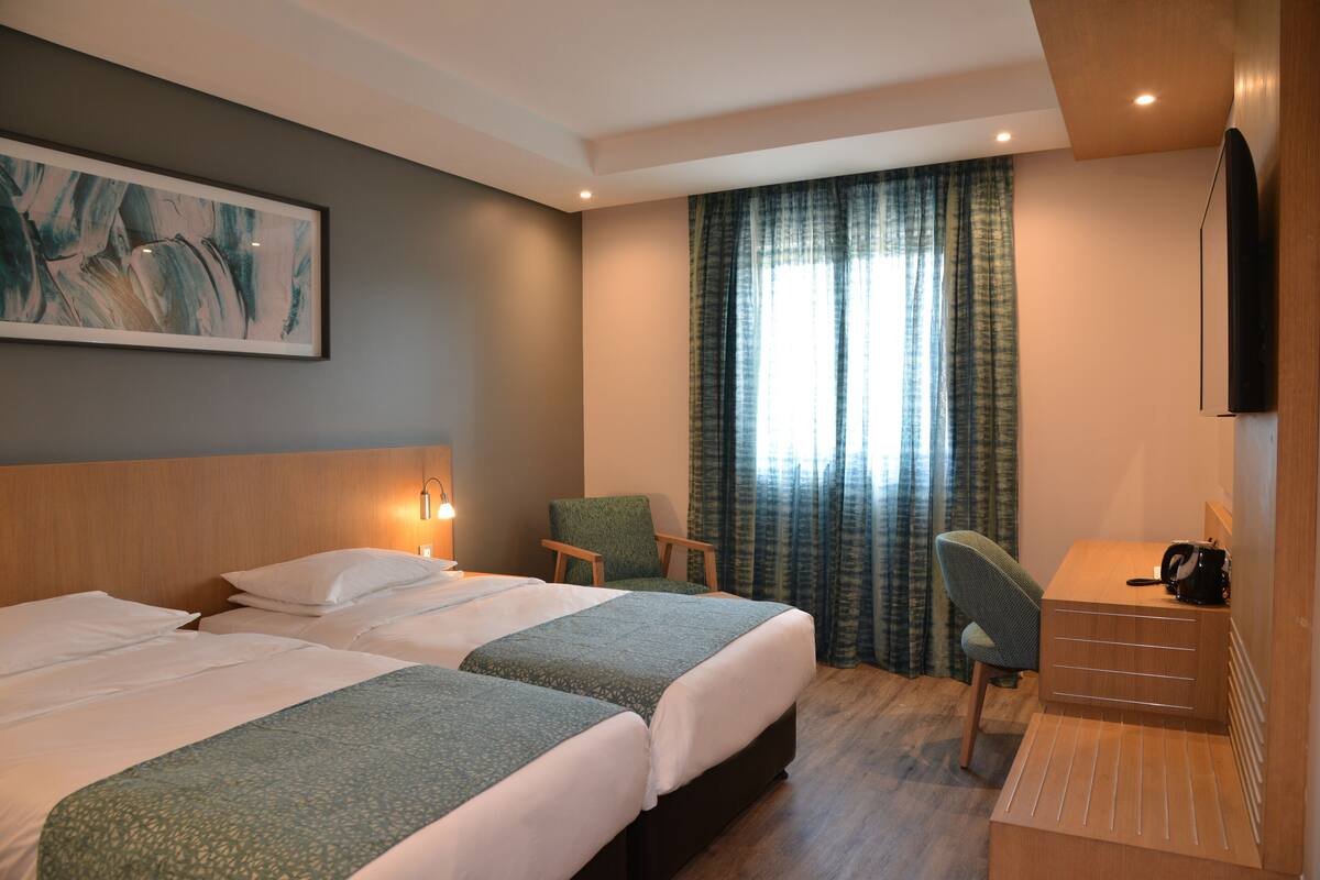 Ein Hotelzimmer mit zwei Betten, einem Schreibtisch, einem Sessel, einem Fernseher und einem Bild an der Wand.