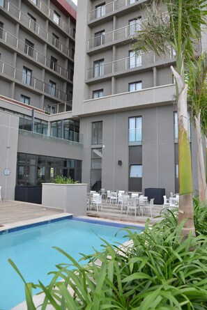 Um edifício moderno com área de piscina, espaço para sentar ao ar livre e escadaria que leva a um balcão superior.