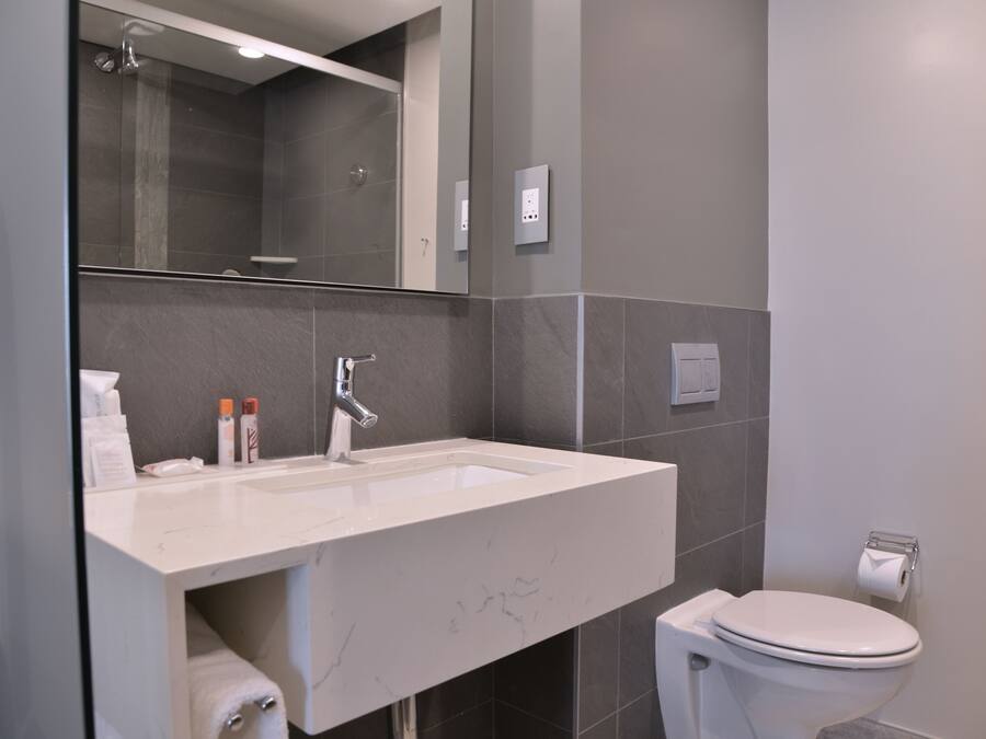 Un baño moderno con lavamanos, espejo y retrete blancos.