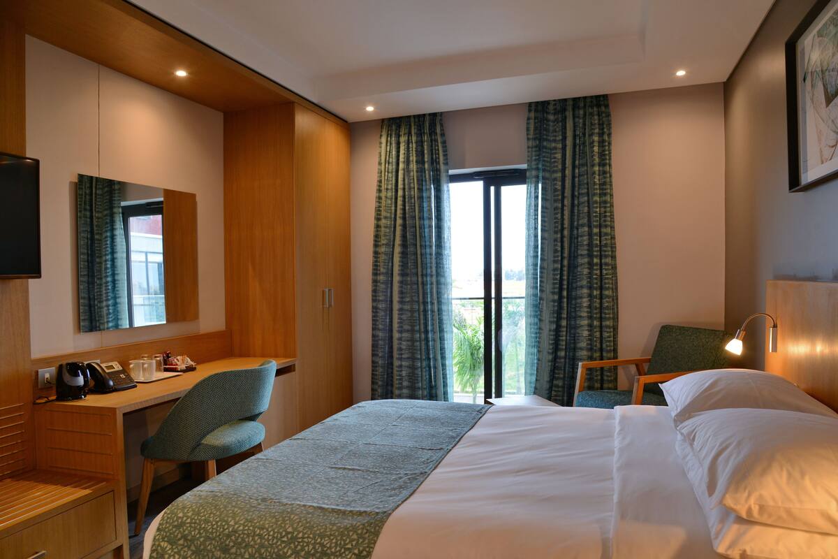 Ein Hotelzimmer mit Bett, Schreibtisch, Stuhl, Fernseher und einem Fenster mit Vorhängen.