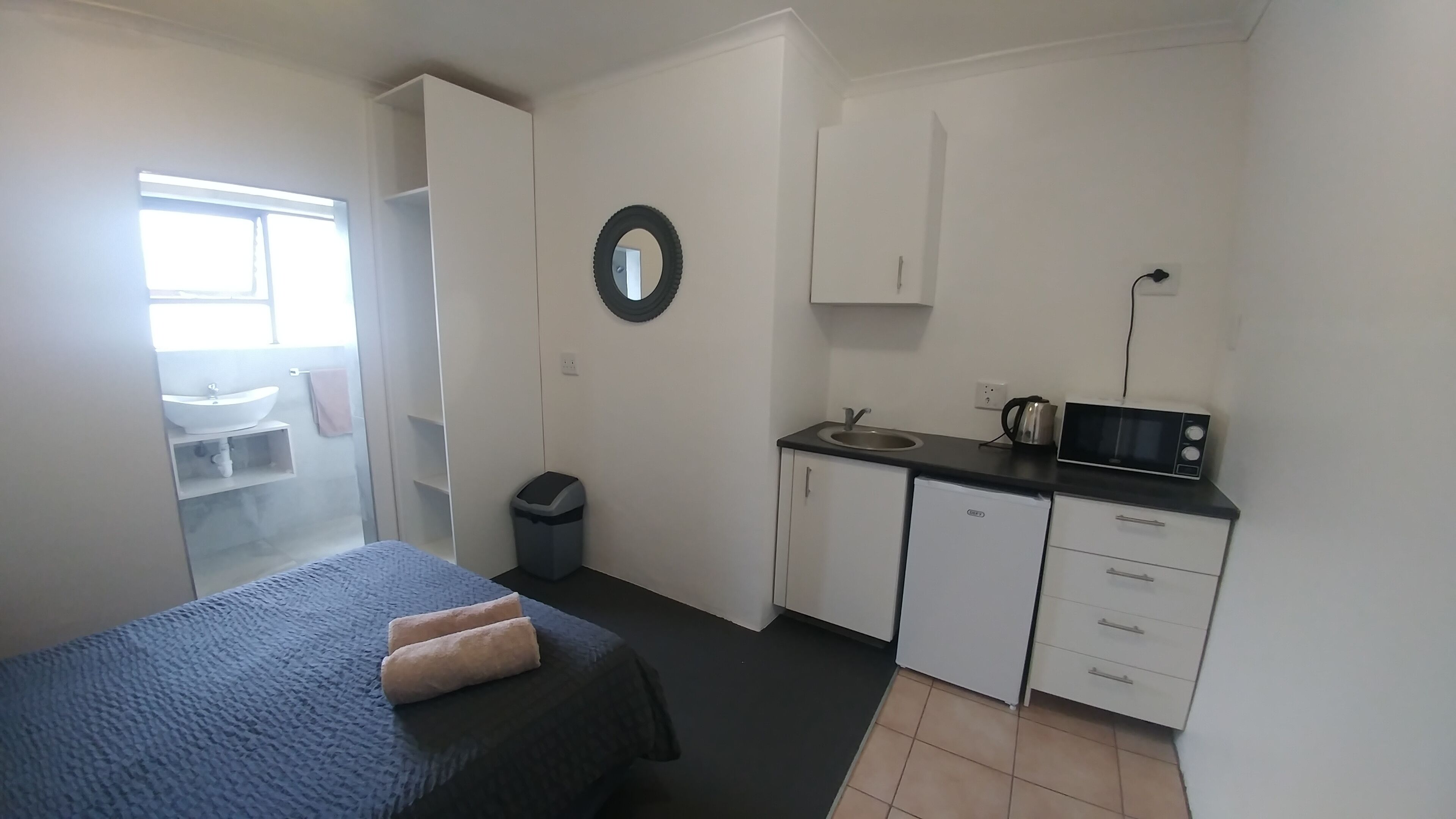A compact room with a bed, a small kitchenette, a bathroom, and a window.