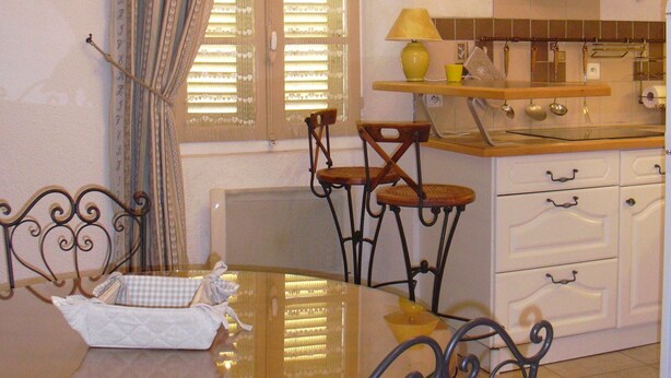 A dining area with a glass table, metal chairs, a window with blinds, a kitchen with white cabinets, and a black range hood. - ANNECY COQUET T2 FURNITURE, NEAR LAKE, OLD TOWN, 2 BIKES (Annecy)
