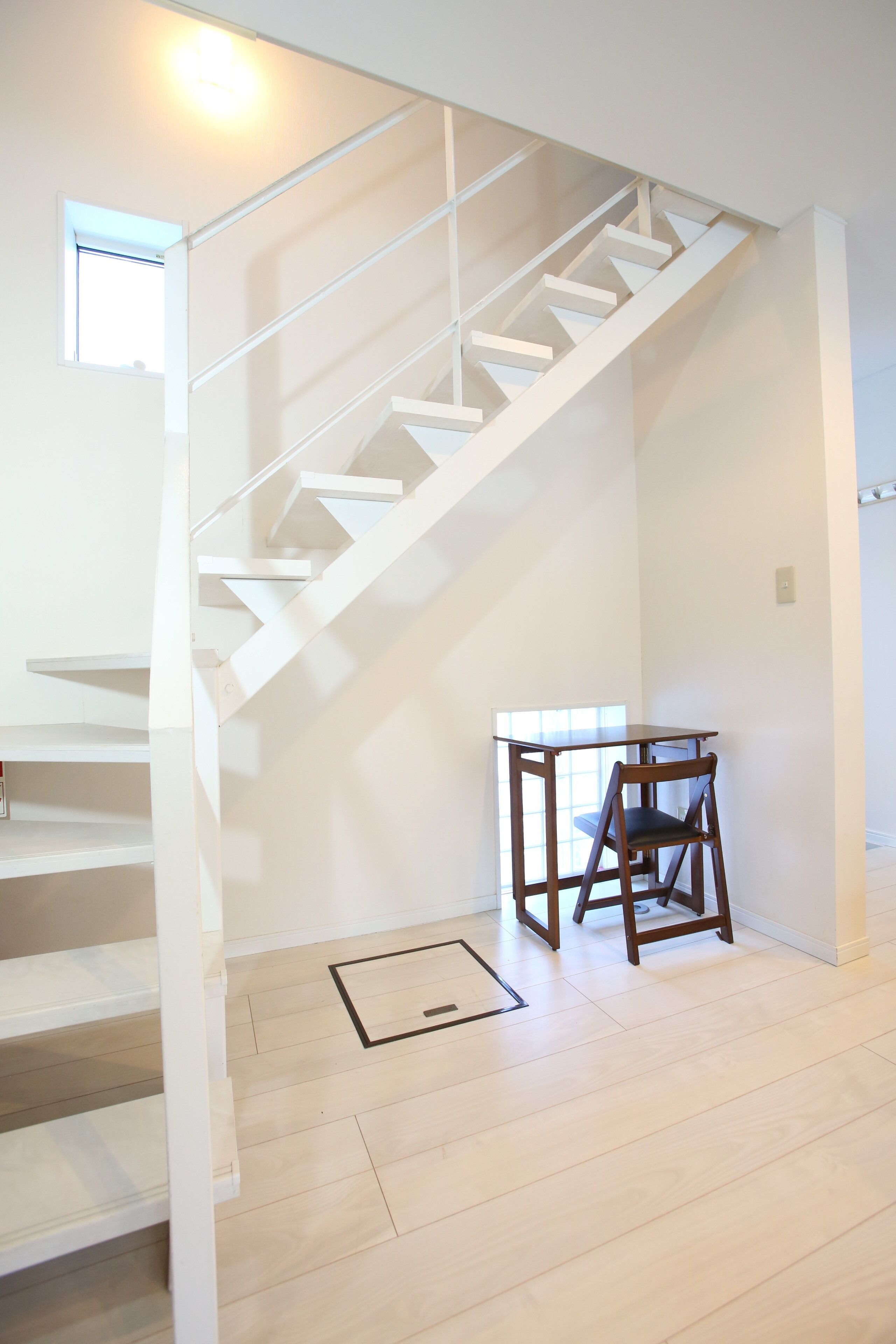 A staircase with white railings, a small table with a chair, and a window with natural light.