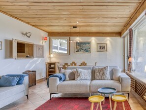 A cozy living room with a wooden ceiling, a sofa, a coffee table, and a window with curtains.