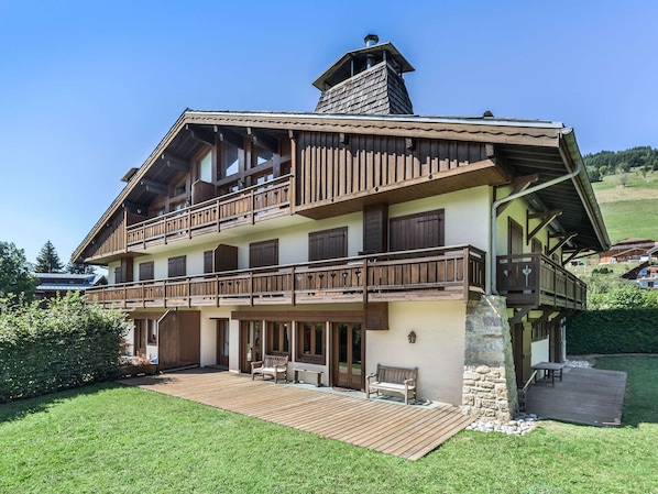 A two-story chalet with a wooden balcony, stone foundation, and a chimney.