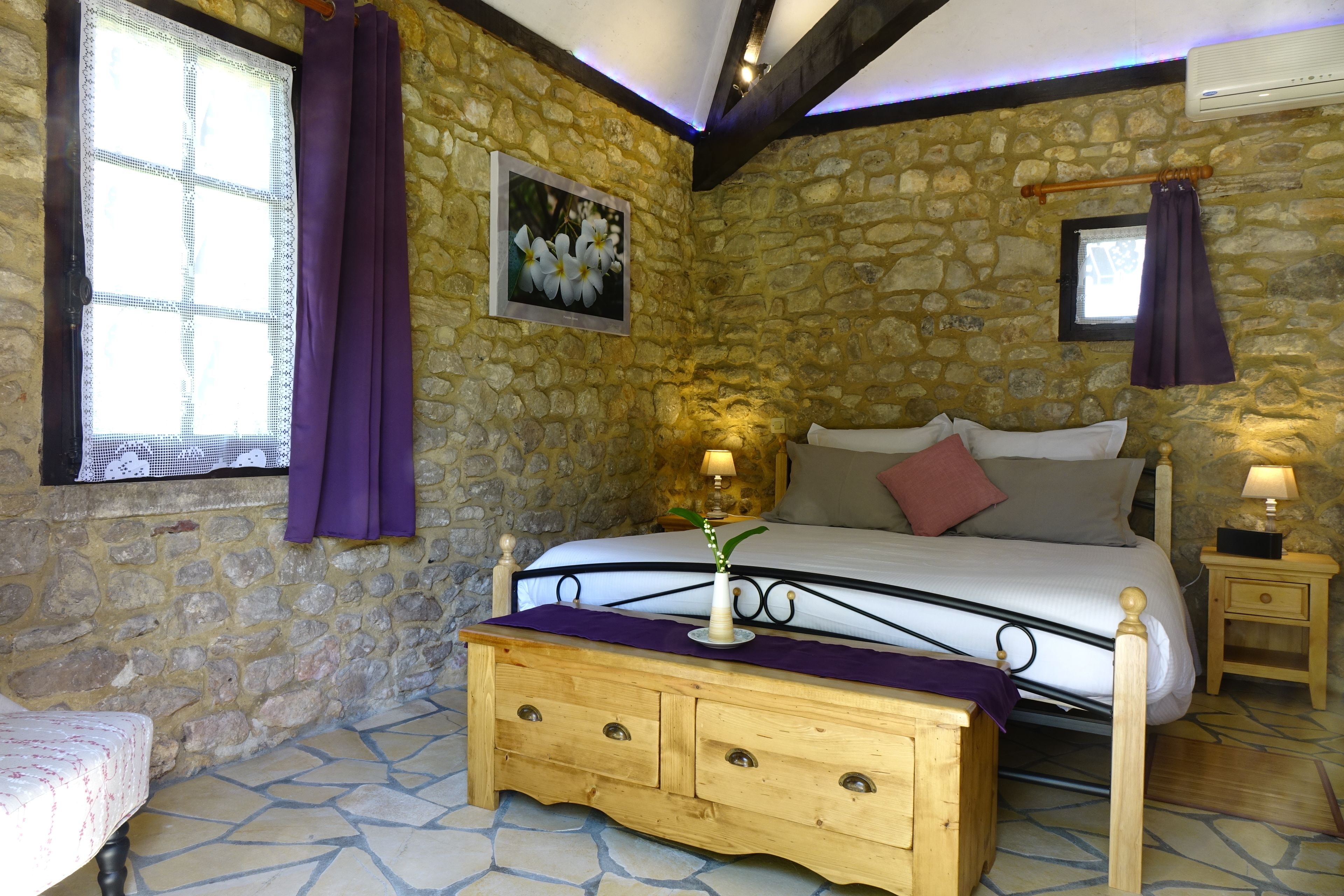 Een slaapkamer met stenen muren, een bed, nachtkastjes en een houten dressoir.