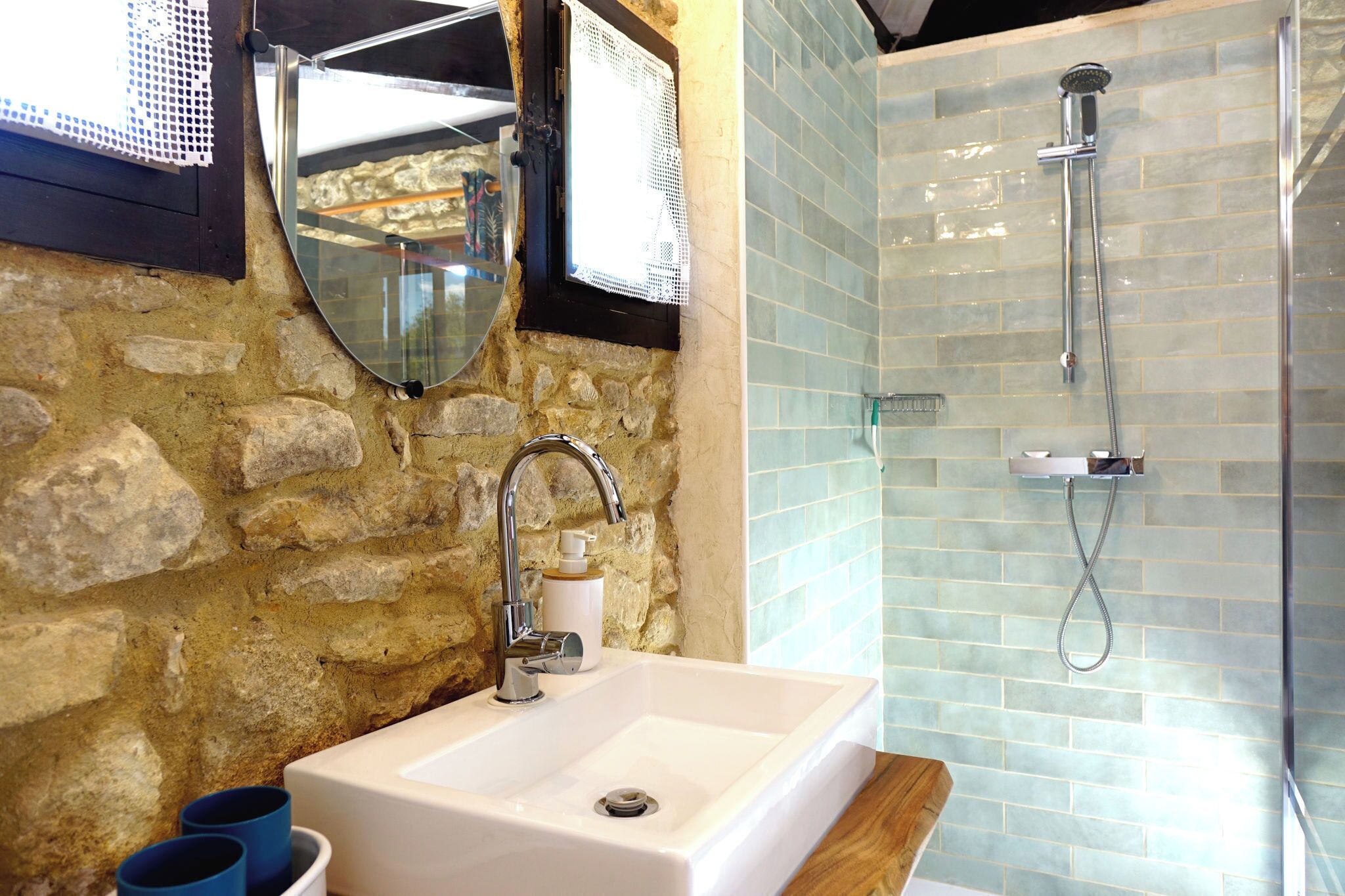 Un bagno con parete in pietra, un lavandino con dispenser di sapone, uno specchio e una doccia con porta in vetro.
