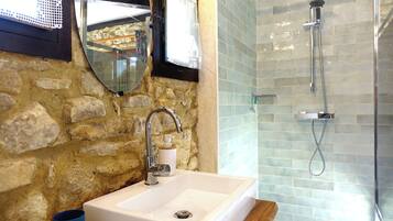 Un bagno con parete in pietra, un lavandino con dispenser di sapone, uno specchio e una doccia con porta in vetro.
