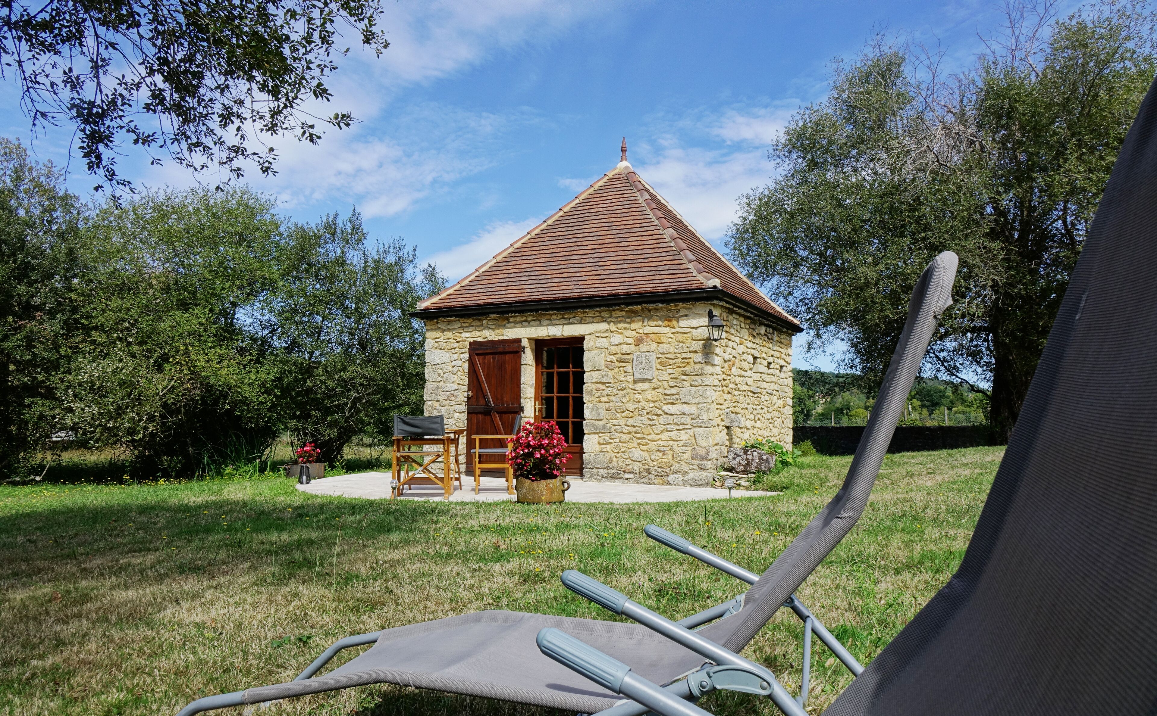 A stone cottage with a tiled roof, a wooden door, and a small porch with a table and chairs.