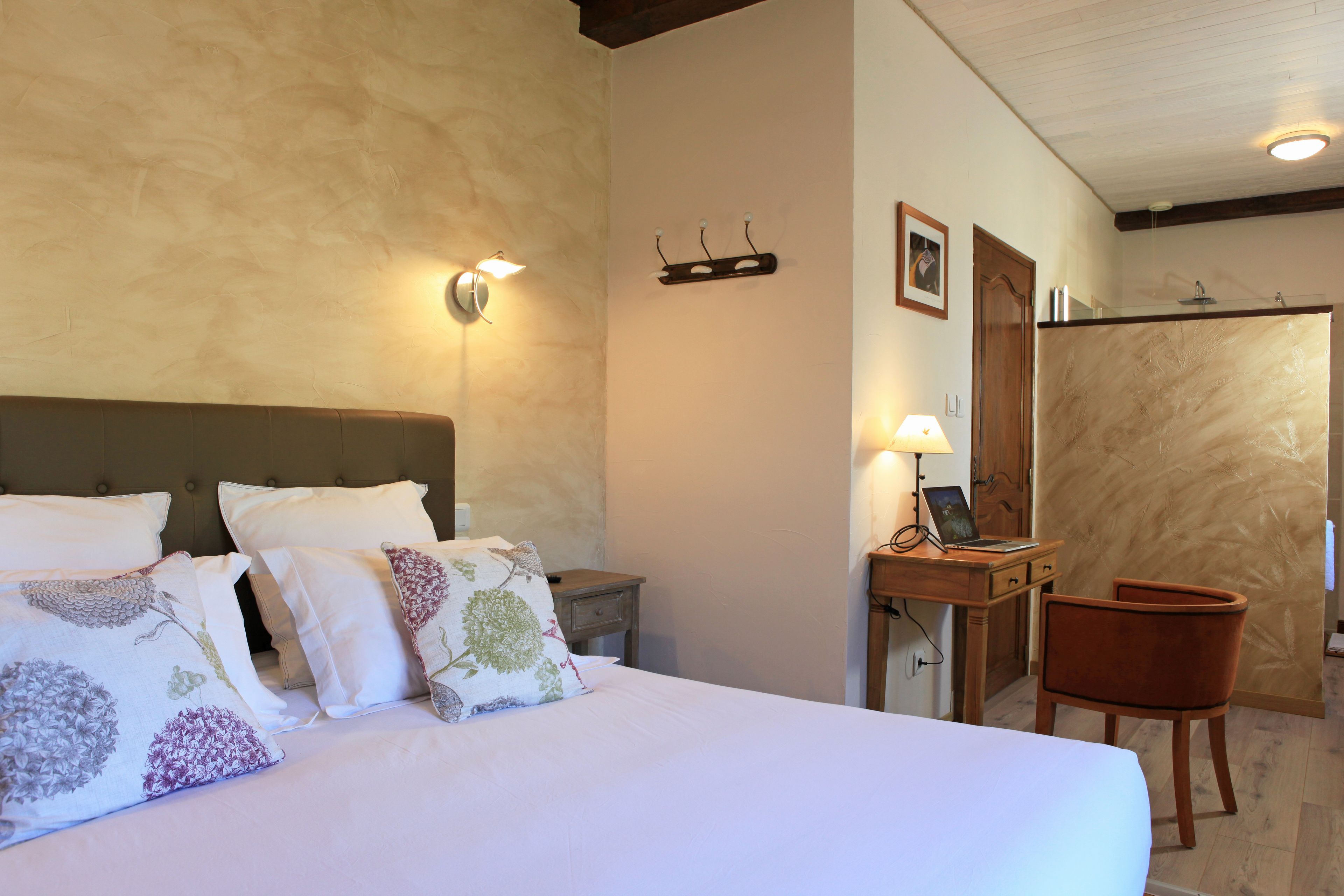 A hotel room with a large bed, a wooden nightstand, a desk with a chair, and a mirror.
